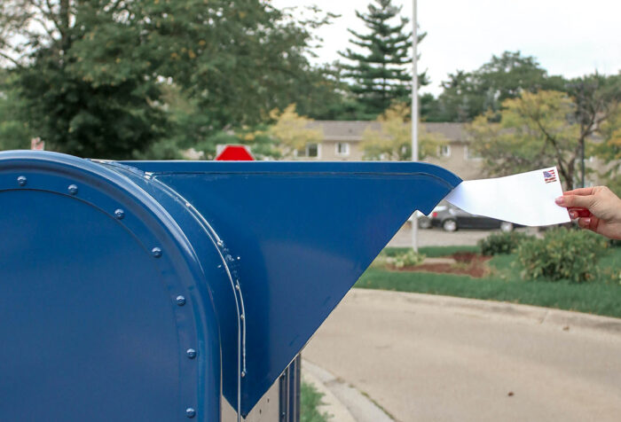 hand inserting envelope with U.S. flag stamp into U.S. mailbox