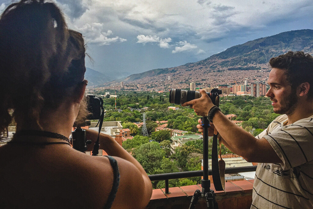 students adjust cameras on balcony with unidentified international city, mountains in background