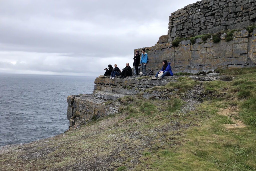 students sit on cliffs overlooking the ocean