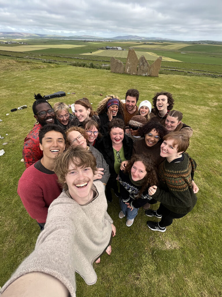 group of students takes selfie in green field, stone formations in background
