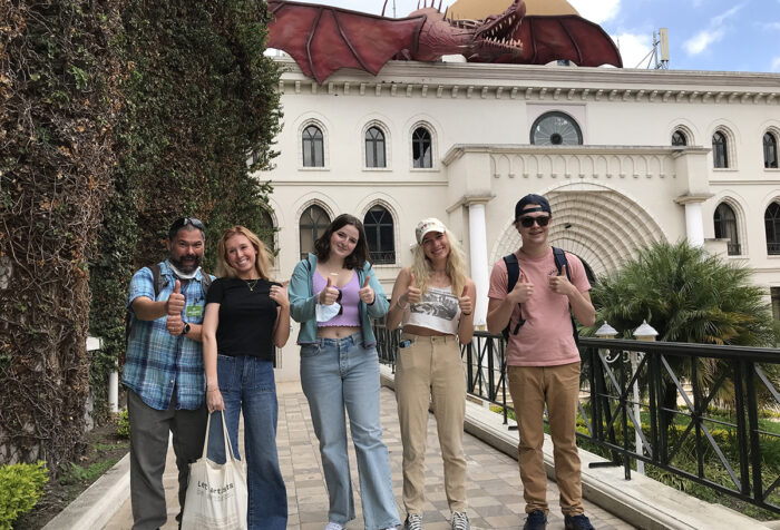 professor and four students give thumbs up in front of white stone building in Quito, Ecuador