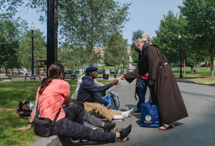 monk in robes hands something to man sitting on curb in Boston Common