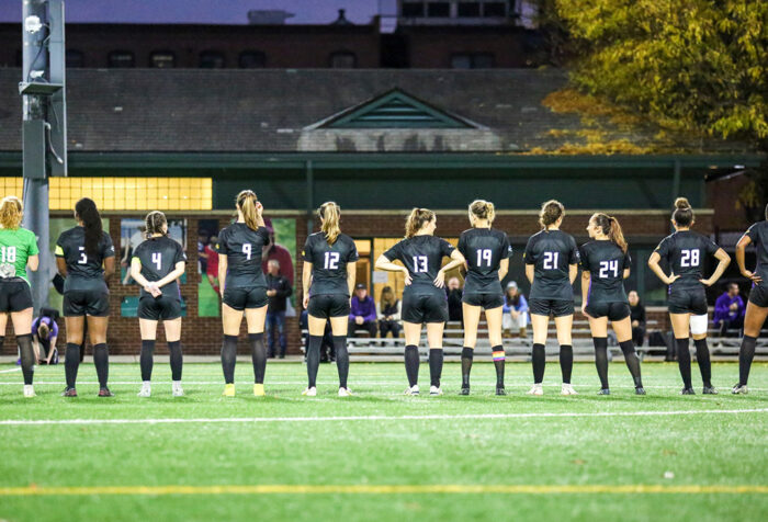 Women's soccer team stand in a row facing the other direction