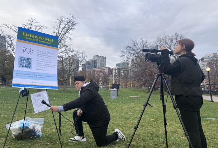 students set up recording equipment in a park, facing a large poster