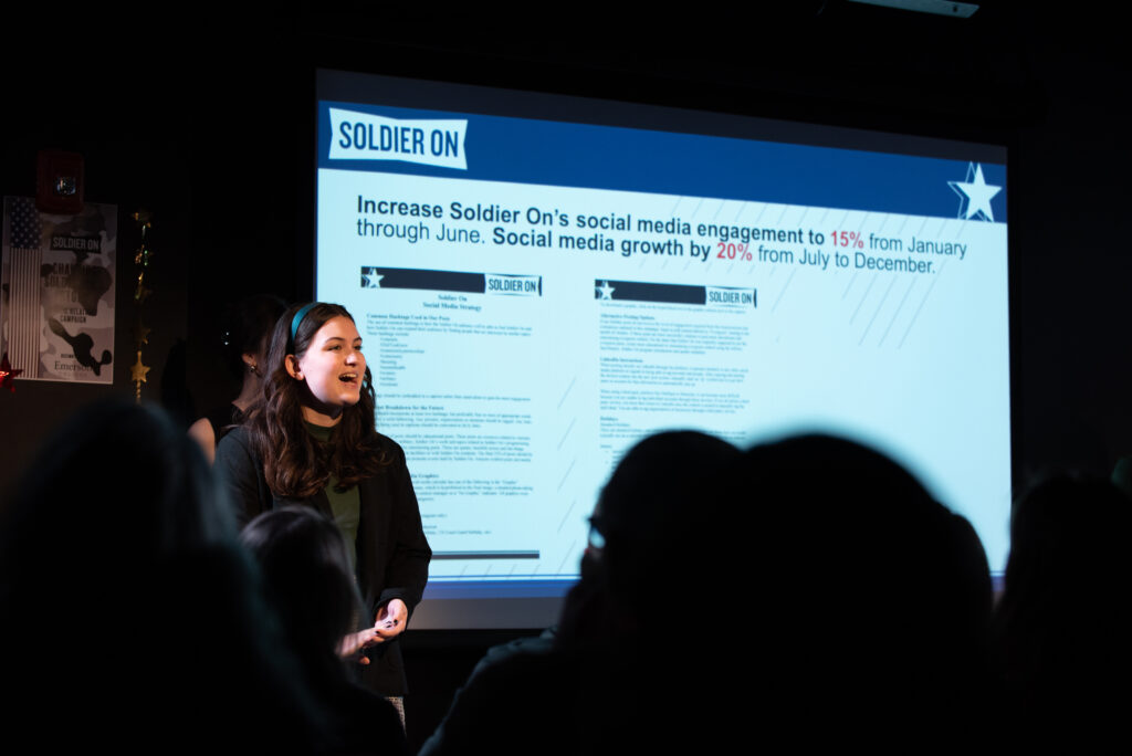 Woman speaks in front of screen showing statistics in darkened room