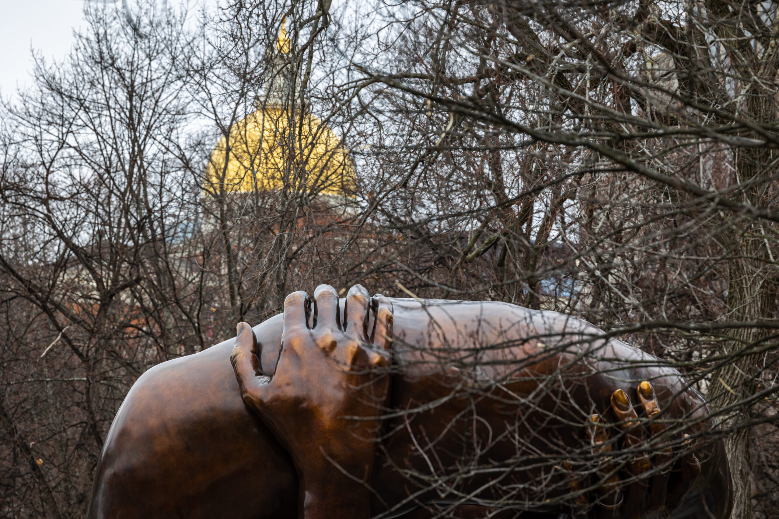 The golden dome of the Massachusetts State House is seen in the background of The Embrace