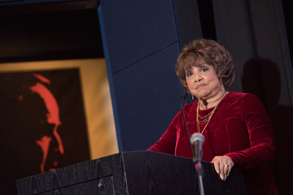 black woman in red velvet dress speaks at podium