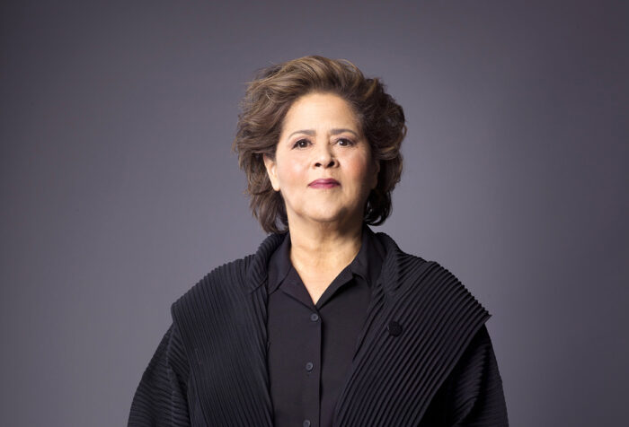 Anna Deavere Smith in black shirt and coat in front of grey background