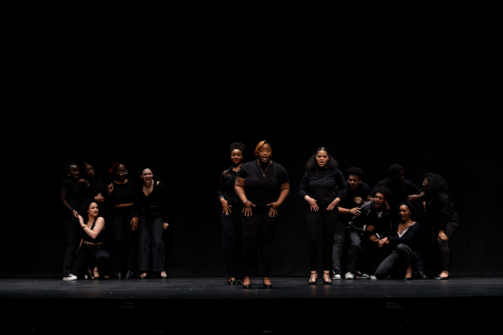 A group of performers in all black on stage
