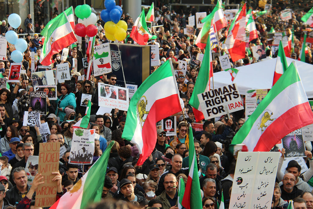 protestors hold signs and Iranian flags