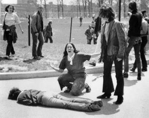 Mary Ann Vecchio kneels, arms outstretched, mouth open, over body of Jeff Miller, lying face down on pavement as college students stand around and look at scene