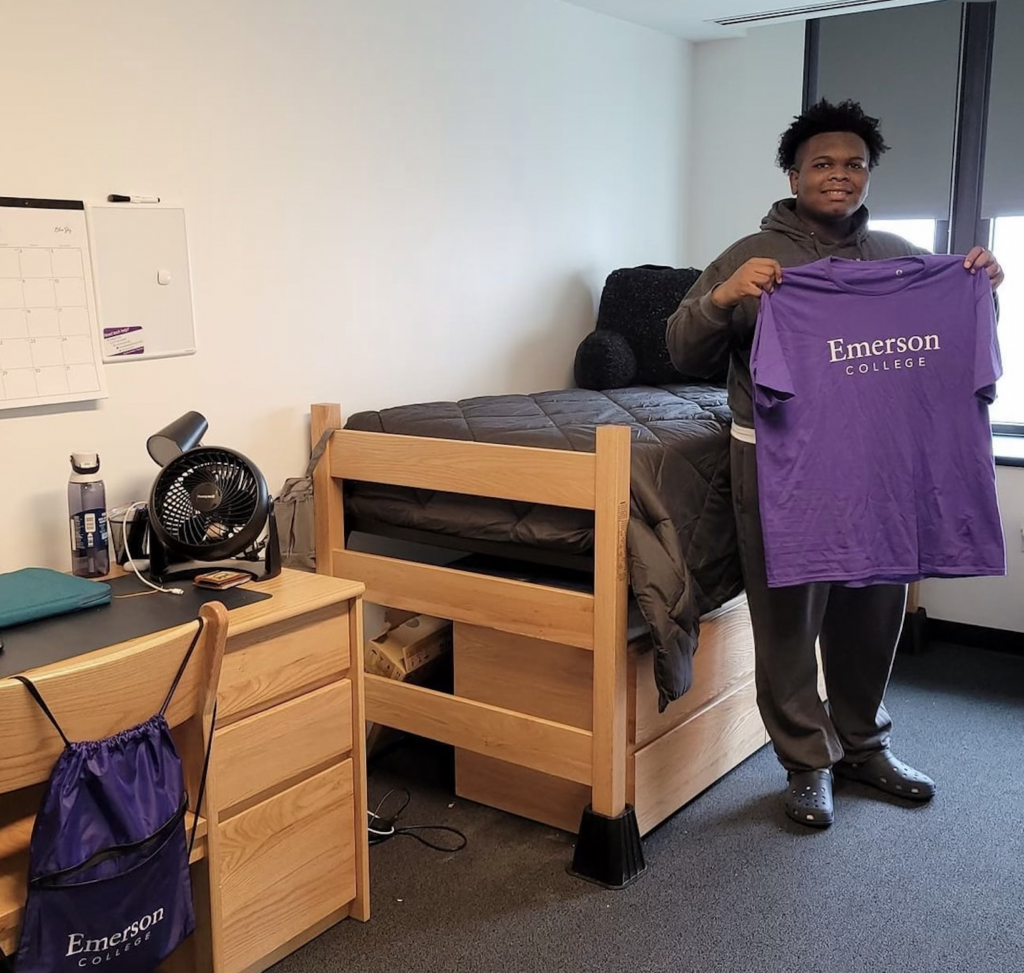 Brooks Walker in his dorm proudly holds up an Emerson College t-shirt