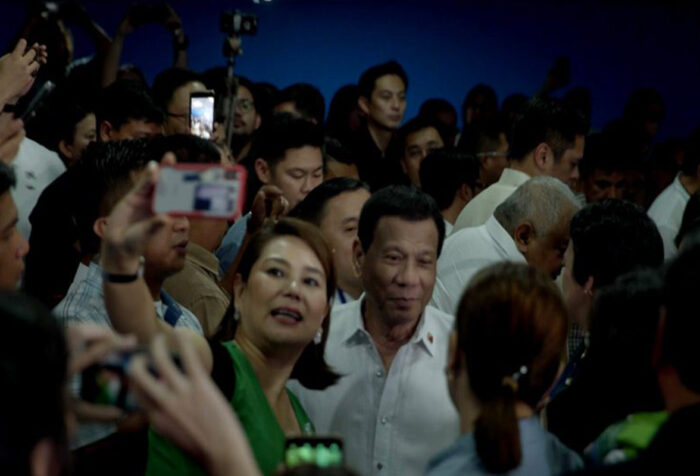 woman in crowd holds up phone to take selfie with duterte