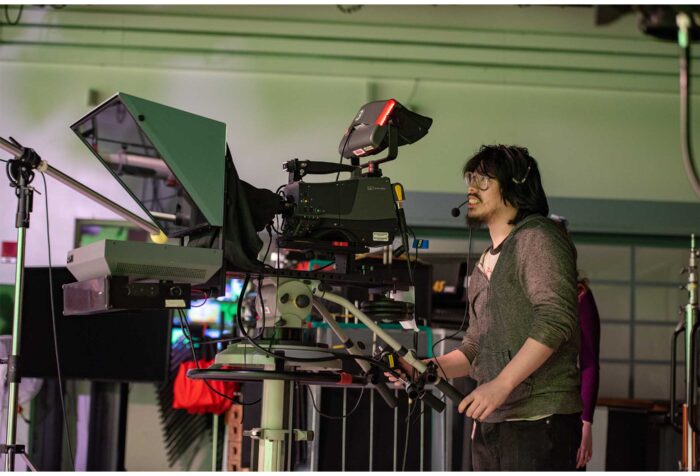 A man looks through a camera, directing a scene