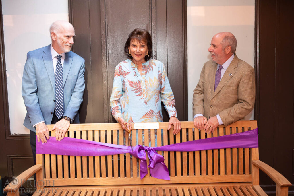Susan Spencer with Interim President Bill Gilligan and another man as she's ready to cut the ribbon for the new bench