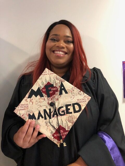 A person holds up their graduation hat that says MFA Managed