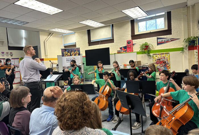 Students perform with string instruments in front of an audience