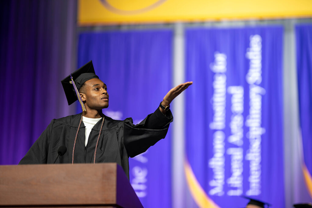 wesley days in cap and gown raises hand from podium