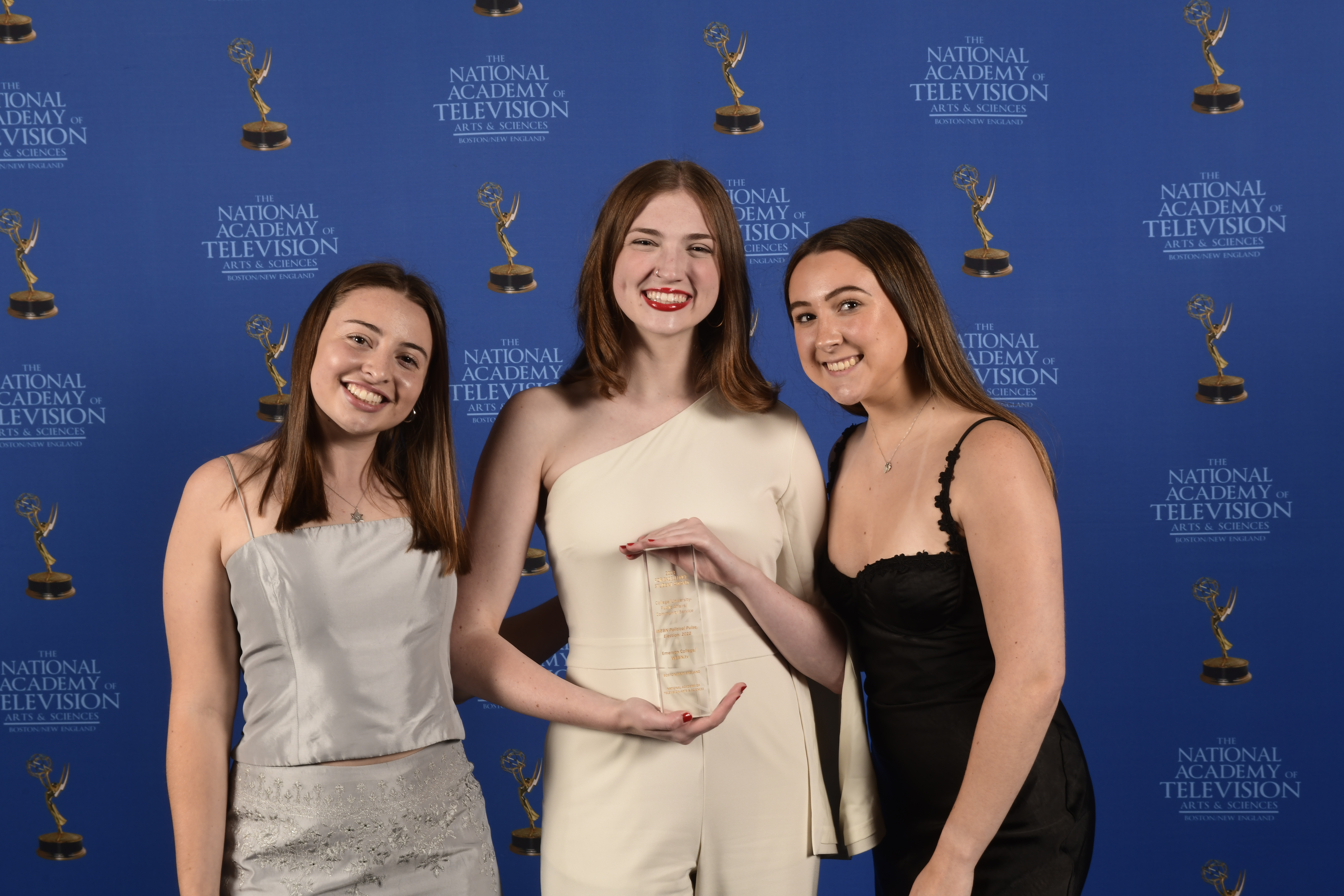 Three women stand together with one in the middle holding an award