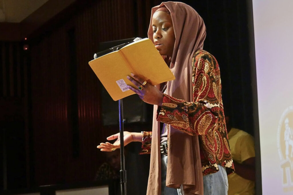 Woman stands at a microphone, reads from a book at