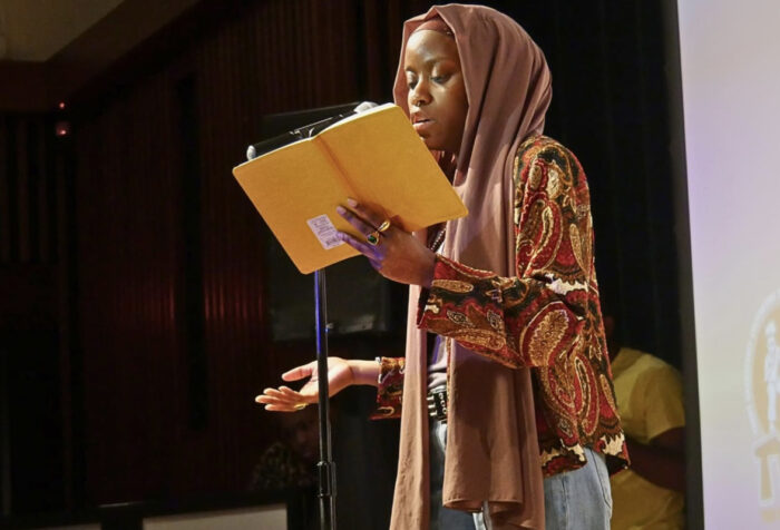 Woman stands at a microphone, reads from a book at