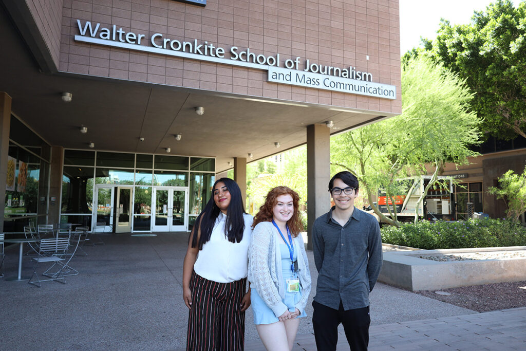 Isa and two other students stand in front of a building with a sign reading Walter Cronkite School of Journalism and Mass Communication. 