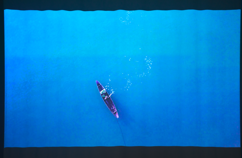 An overhead shot of a person in a single boat in blue water
