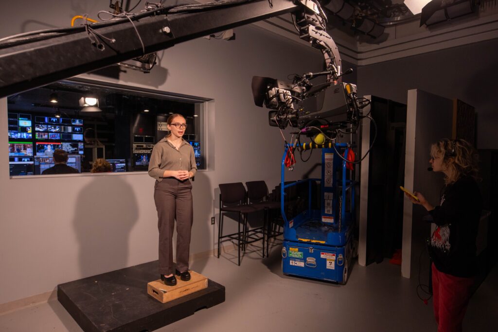 A person stands on a little stage ready to report from the studio