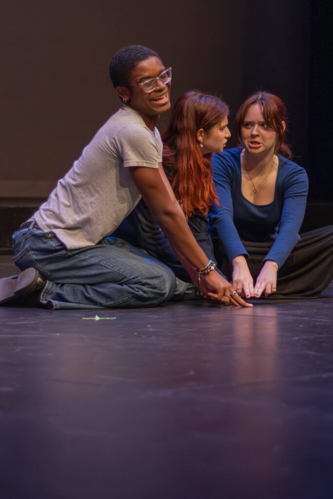 Three people on a stage together put their hands together on the floor