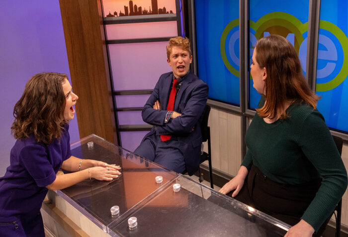 Three people talk around the news desk