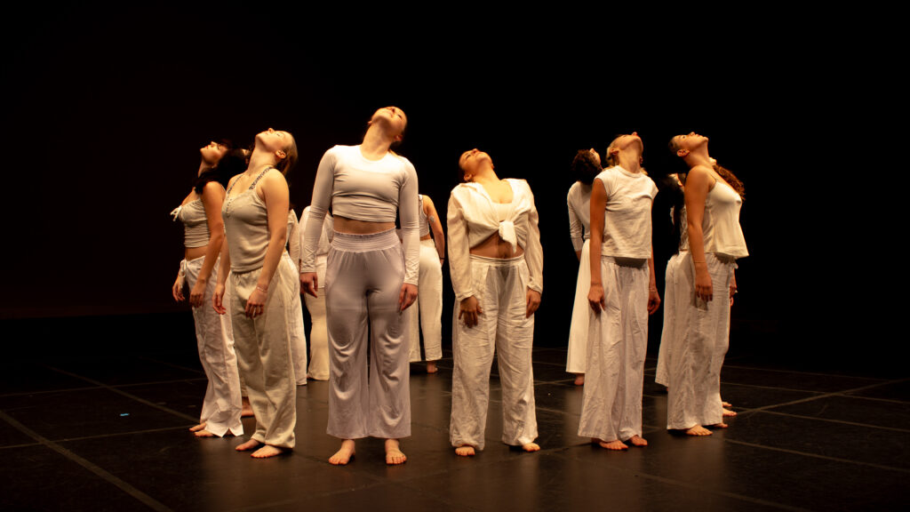 Dancers in all white are on their toes and reach their heads up high
