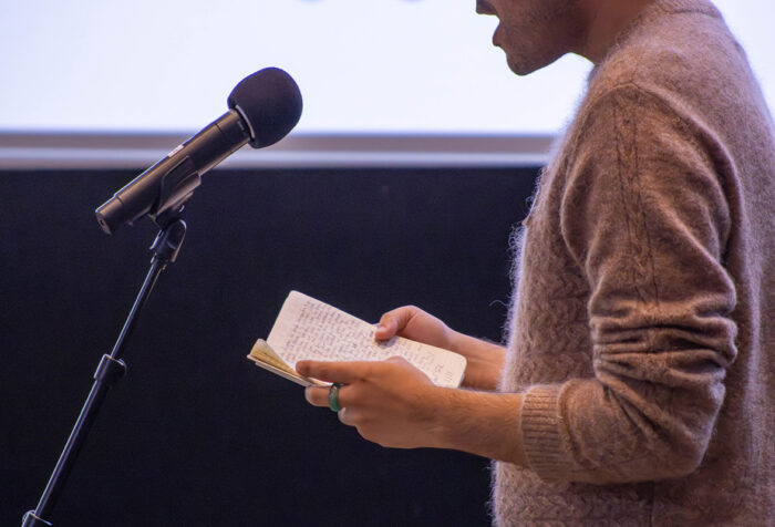 torso of man reading from notebook at microphone