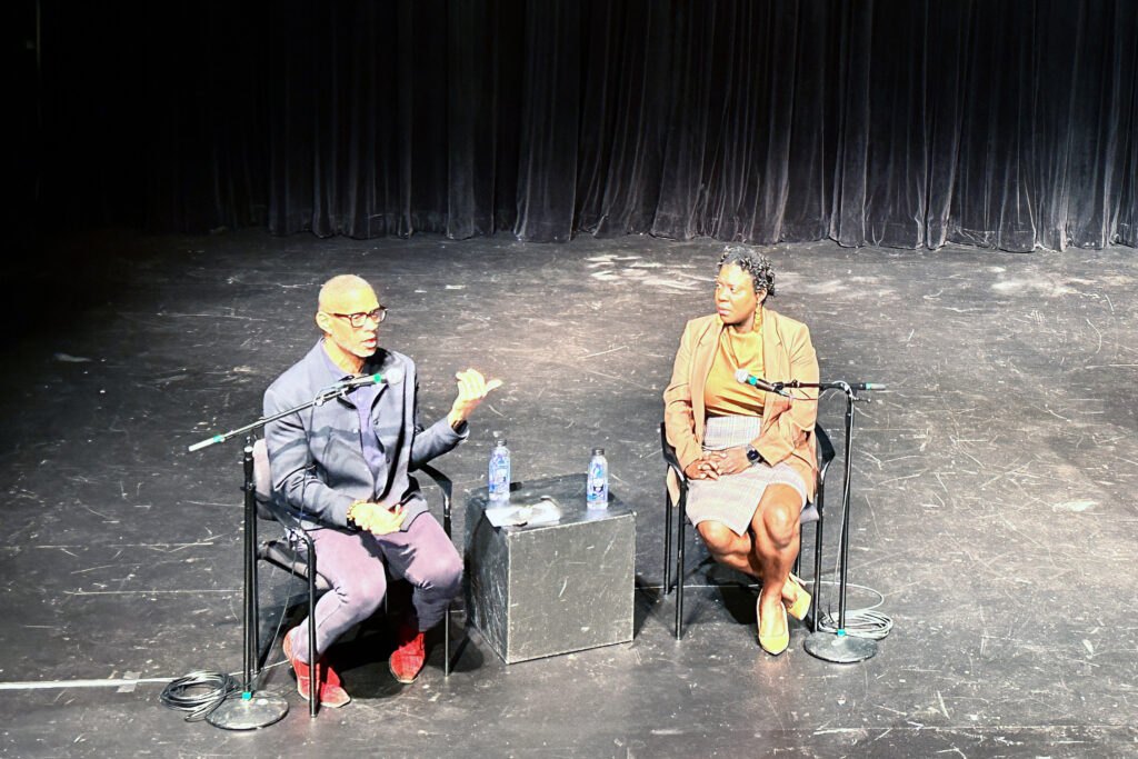 Two people sit on stage during a panel discussion