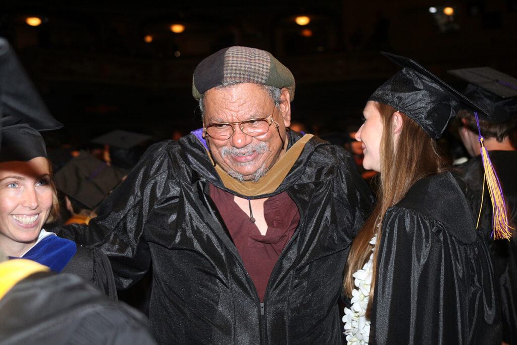 Pierre Desire, in unbuttoned academic robe talks to students