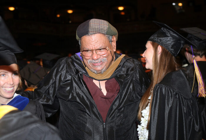 Pierre Desire, in unbuttoned academic robe talks to students