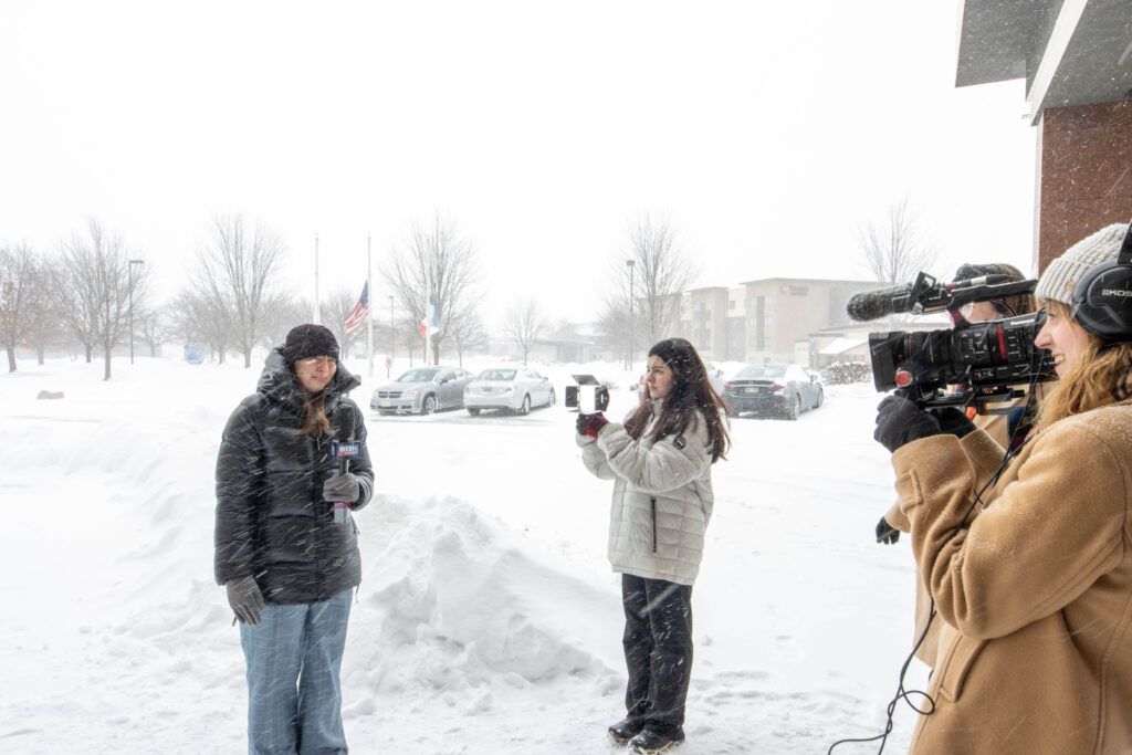 Students stand in the snowy weather to record a video