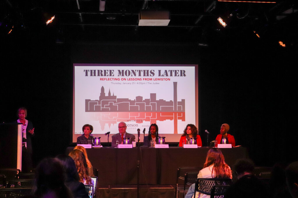 The five panelists sit at a long table, covered in a black tablecloth at the front of the black box theatre.