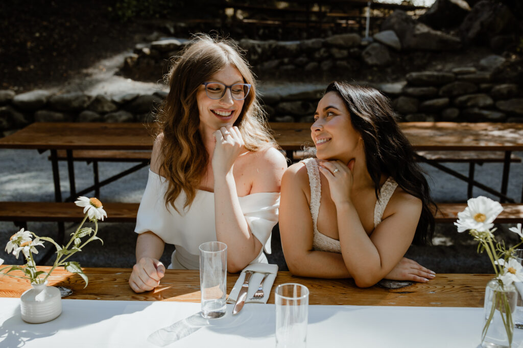 Mara Martin and Jane Martin Dentinger smile and look into each other's eyes while sitting and wearing white wedding dresses