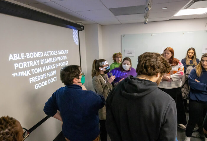 students have a discussion in front of a screen with words projected