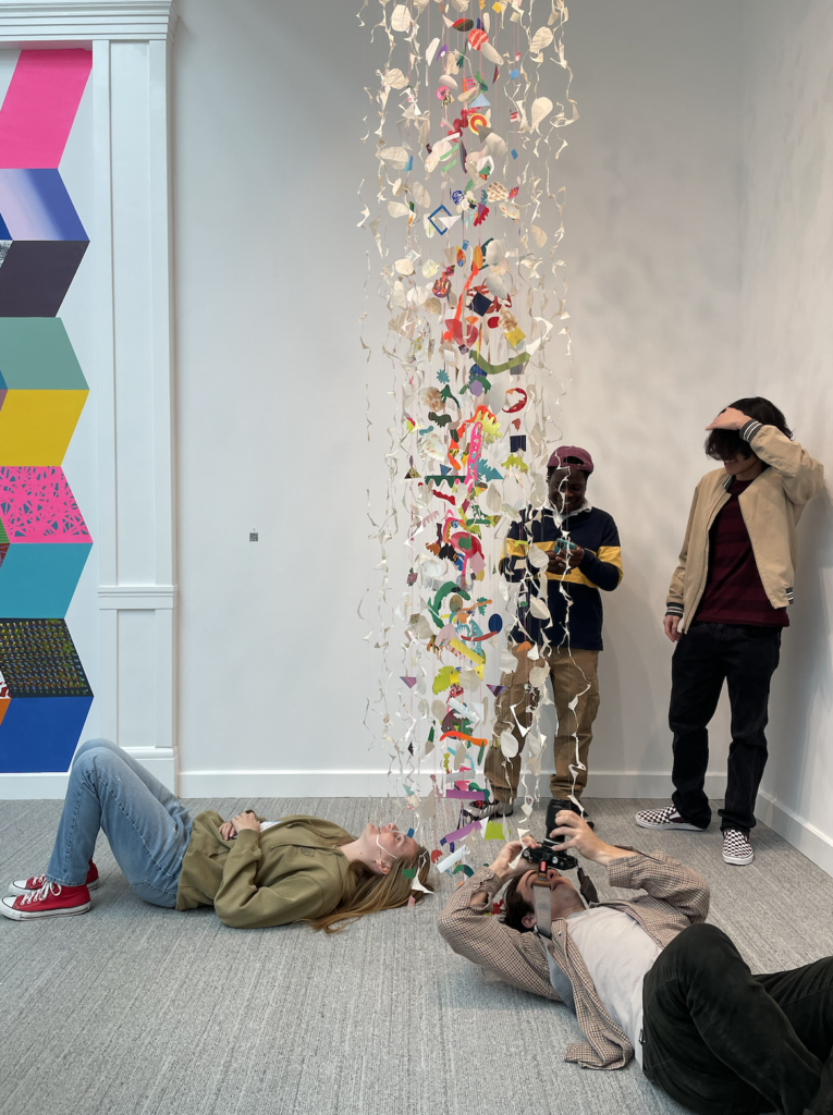 At a field trip taken to an art gallery, two students lay on the ground while two stand against the wall
