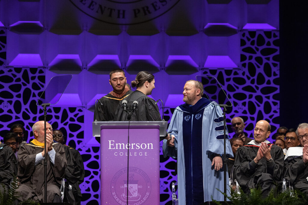 Dr. Bernhardt, in blue robes, shakes hand of young woman as young man looks on.