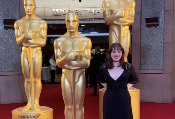 Ruby Brooks stands near three life size Academy Awards