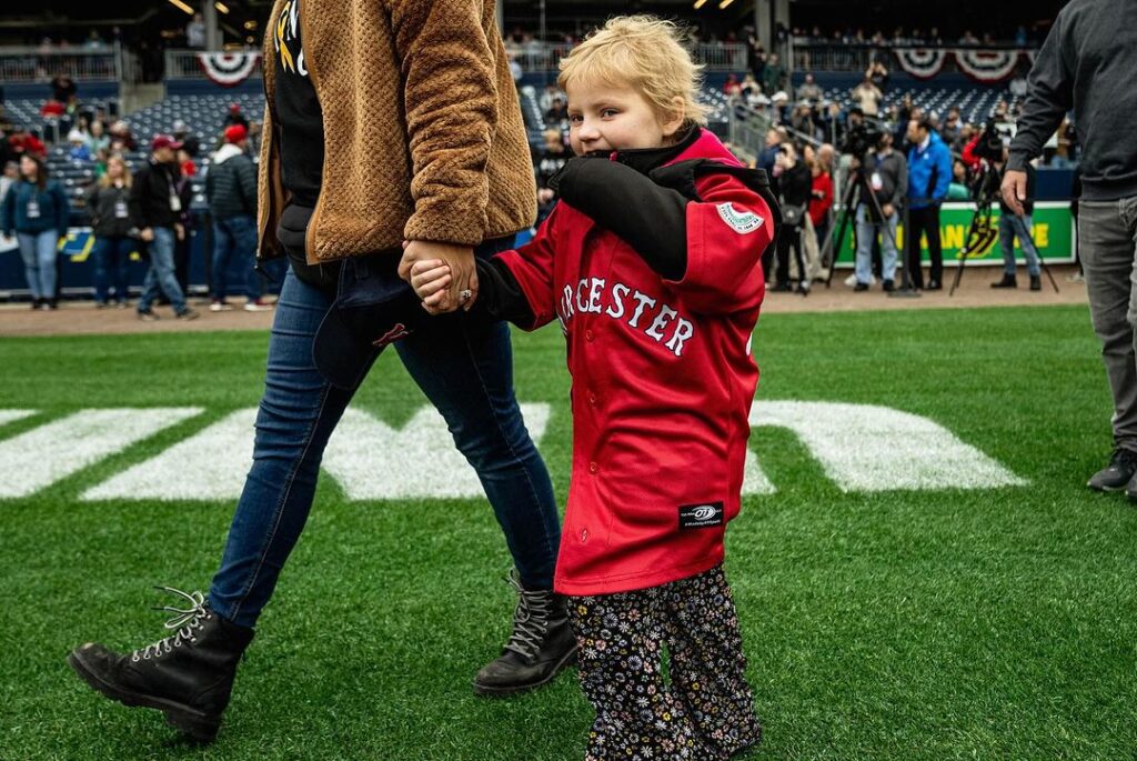 Ava Blazis walking on the field wearing a Worcester WooSox jersey holding her parent's hand