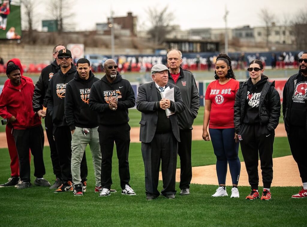 Charles Steinberg and members of two high school basketball teams stand together on the baseball field
