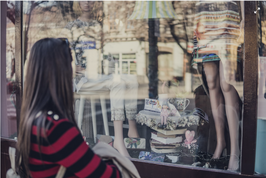 Young outside store front gazes at merchandise and clothing on a window display with mannequins. 