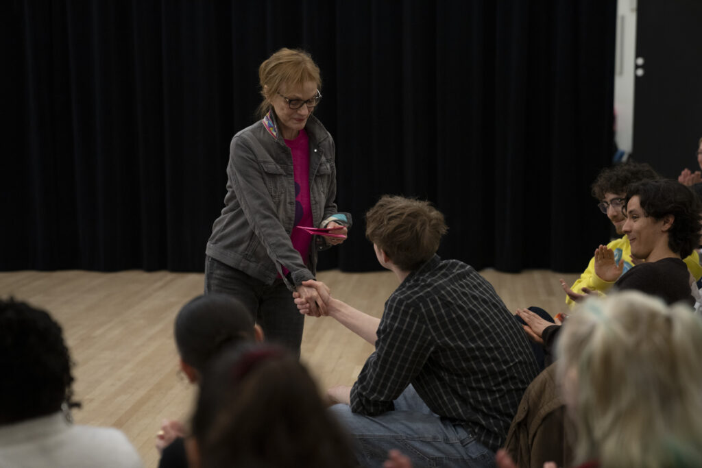 Judee Wales Watson stands while shaking the hand of seated student