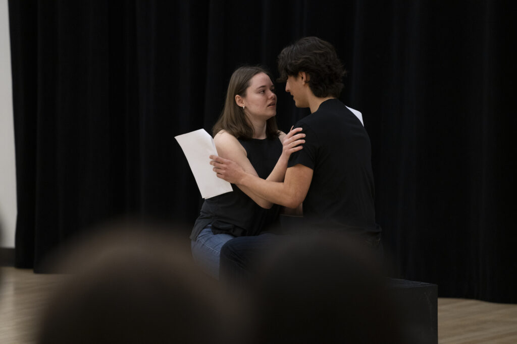Two students sit and embraced while performing a scene.