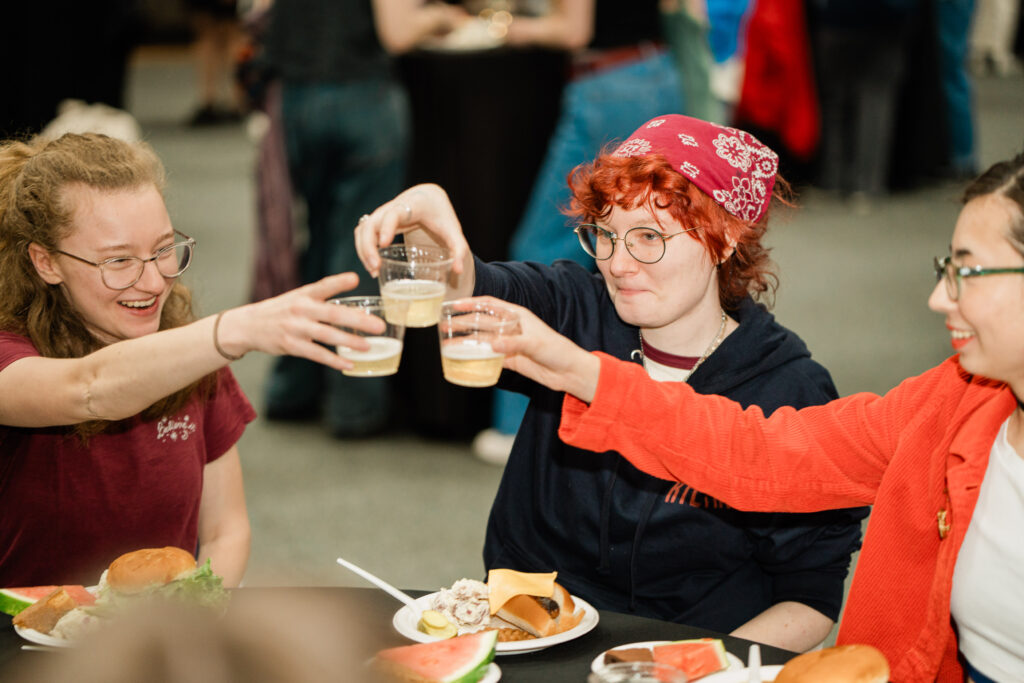 Three people do a toast with drinks in hand and holding plates of food