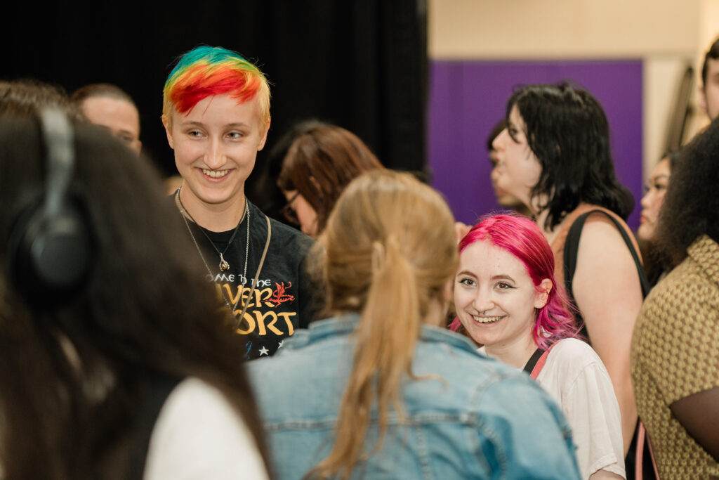 Two people with brightly dyed hair smile while talking to other people
