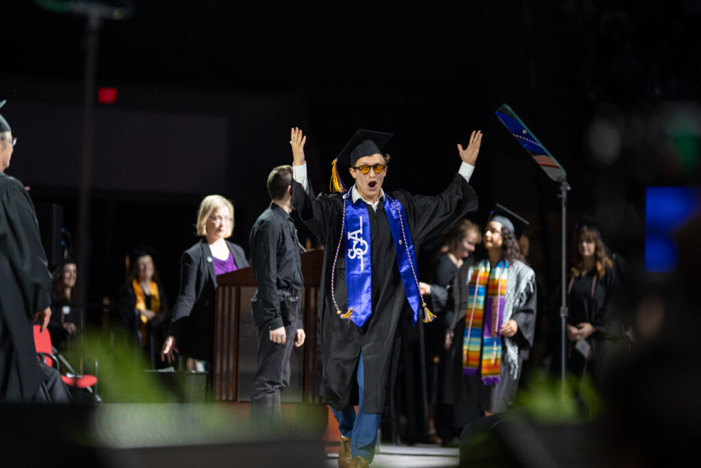 A student raises their hands on the stage after receiving a diploma